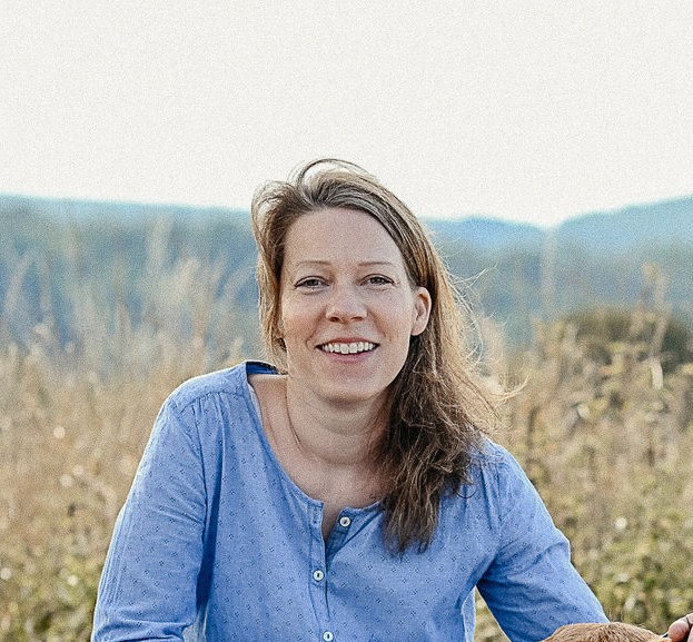 HTA Practitioner Sandra Fischer wearing a blue shirt and sitting in a field.